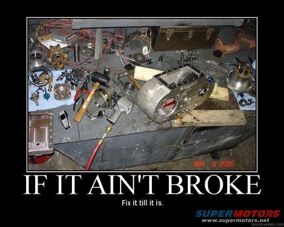 Workbench cluttered with car parts, tools, and wiring. Includes a large metal casing with gears visible inside