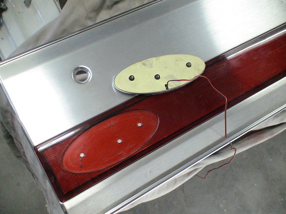 Ford oval emblem removed from tailgate, showing mounting holes and wiring. Red taillight lens visible
