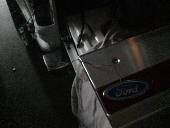 Close-up of a Ford oval emblem on a vehicle's tailgate, with exposed wiring