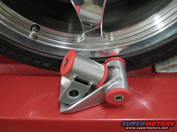 Aftermarket suspension bushings with red urethane inserts next to a tire and chrome wheel