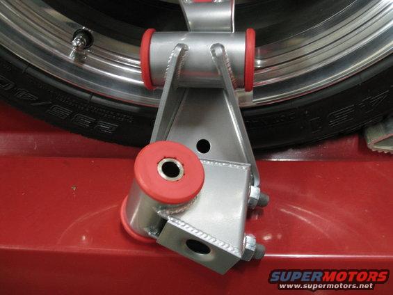 Aftermarket suspension component with red polyurethane bushings next to a tire and wheel