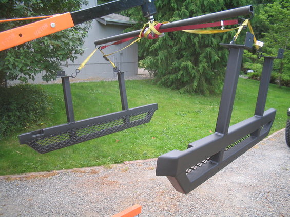Two black metal sliders with mesh inserts suspended by a crane