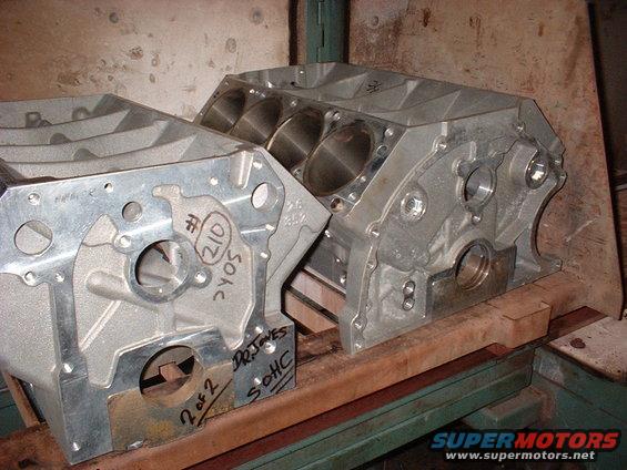 Two aluminum engine blocks are on wooden supports. One block has handwritten markings: '# 210 2YOS' and '2 of 2 DR. JONES SOHC'