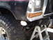 1979 Ford Bronco - Front view of a black Ford truck with a large tire and lifted suspension, showing the fender and turn signal.