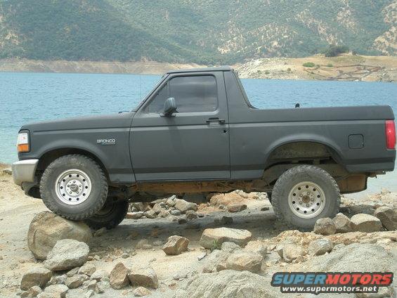 Side view of dark gray 1990s Ford Bronco on rocks near water