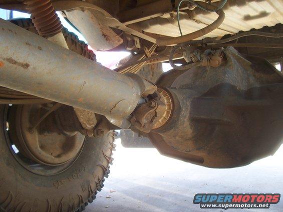Driveshaft and differential of a truck, showing rust and wear. Visible U-joint and rear axle housing