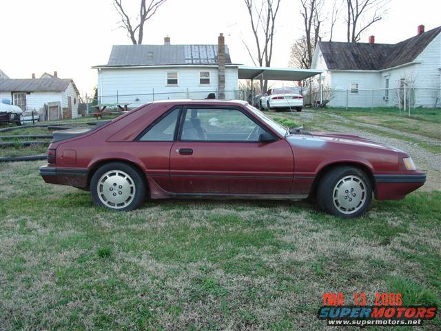 Red 1984 Ford Mustang coupe parked on grass, side view