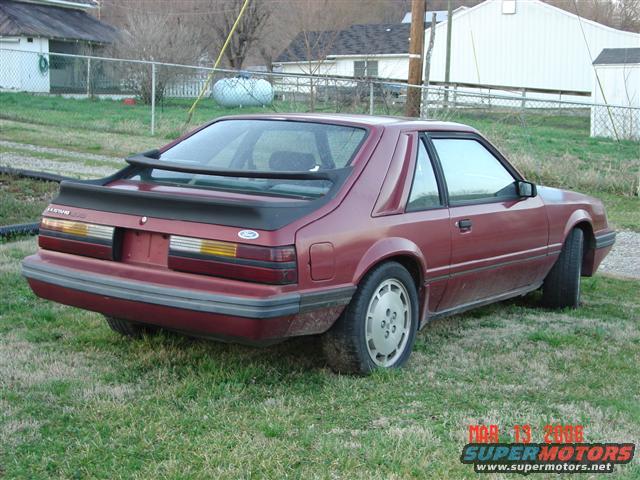 Red 1984 Ford Mustang coupe, rear 3/4 view, parked on grass