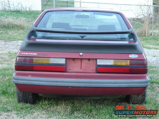 1984 Ford Mustang rear view, red hatchback with black spoiler and "MUSTANG 5.0" badge
