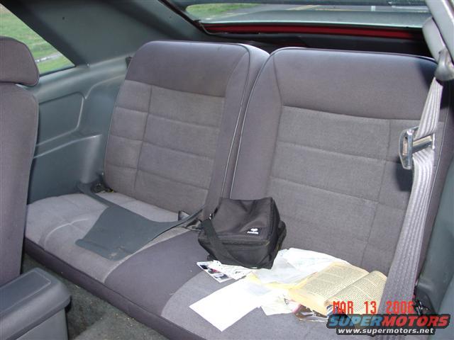 Back seat of a car with gray fabric seats, a black bag, and an open book on the seat. A watermark reads "MAR 13 2006 SUPERMOTORS.NET"