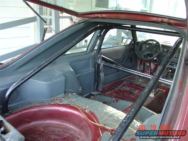 Interior of a car with a roll cage, stripped-down rear seating area, and a dashboard with a steering wheel