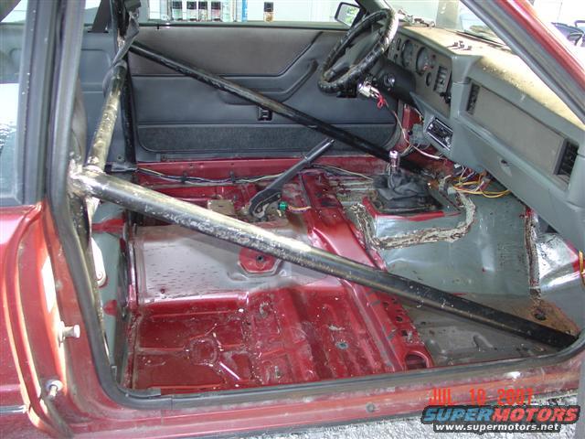 1984 Ford Mustang interior stripped down with roll cage installed, manual transmission shifter visible