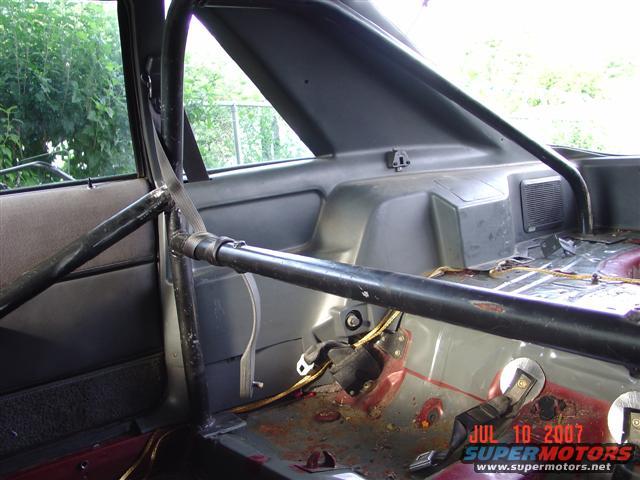 Interior view of a car with a black roll cage and racing seatbelt
