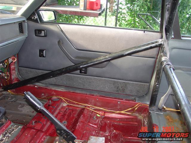 Interior of a car with a roll cage, stripped-down floor, and door panel