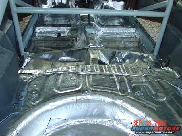 Car interior floor covered in silver sound deadening material, with a roll cage visible