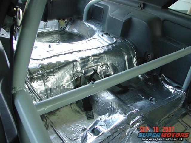 Car interior with sound deadening material on the floor and rear panels. Roll cage installed