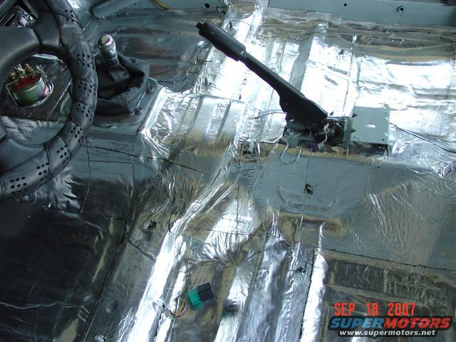 Car interior showing sound deadening material on the floor, a steering wheel, and a manual shifter