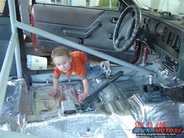 Kid crawling on floor of car with sound deadening material installed. Roll cage visible