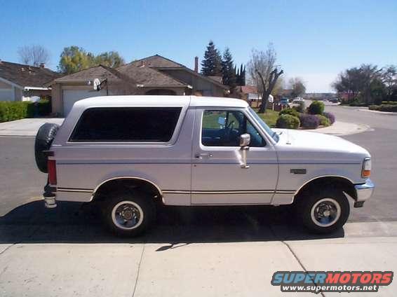 White Ford Bronco parked on a suburban street, side view. Spare tire mounted on the back