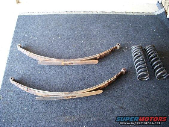 Two leaf springs and two coil springs on a dark carpeted surface