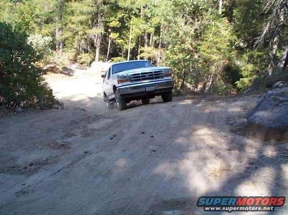 White Ford Bronco driving on a dirt road, front 3/4 view