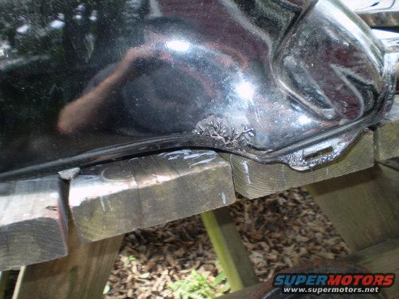 Black motorcycle fuel tank with rust damage on the lower edge, resting on wooden blocks