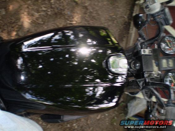 Black motorcycle fuel tank with reflections, showing part of the handlebars and gauges