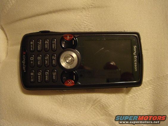 Black Sony Ericsson mobile phone with a keypad and screen, lying on a textured surface