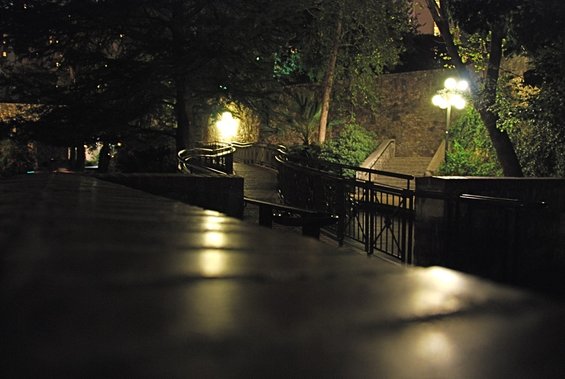 Night view of a stone wall, trees, and a curved walkway with lights reflecting on the wet surface