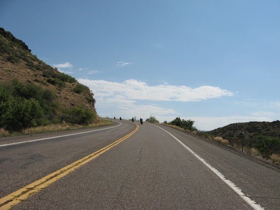 Motorcycles on a winding road with a mountain on the left and hills on the right