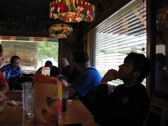 Interior scene with people at a table, stained glass lamps overhead, and blinds covering a window