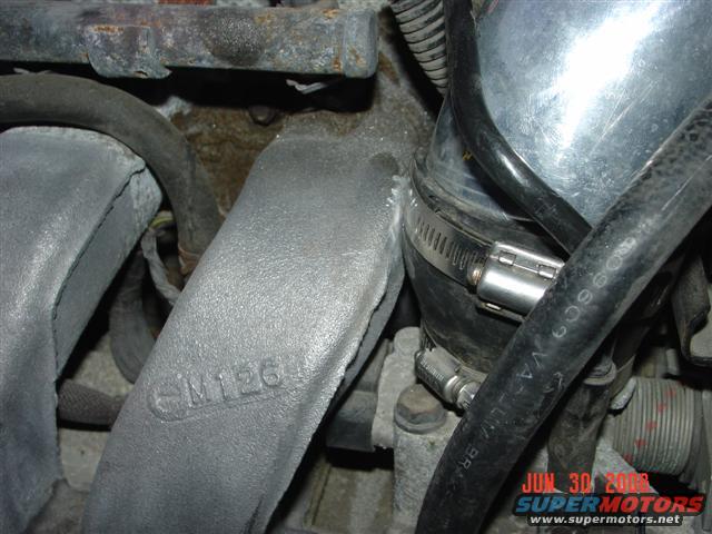 Engine intake manifold with "M126" casting mark, metal hose clamp, and black hoses