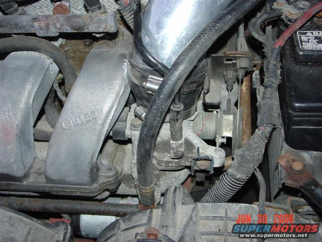 Close-up of engine throttle body, intake manifold, and battery connections. Text 'GM 120' visible on manifold