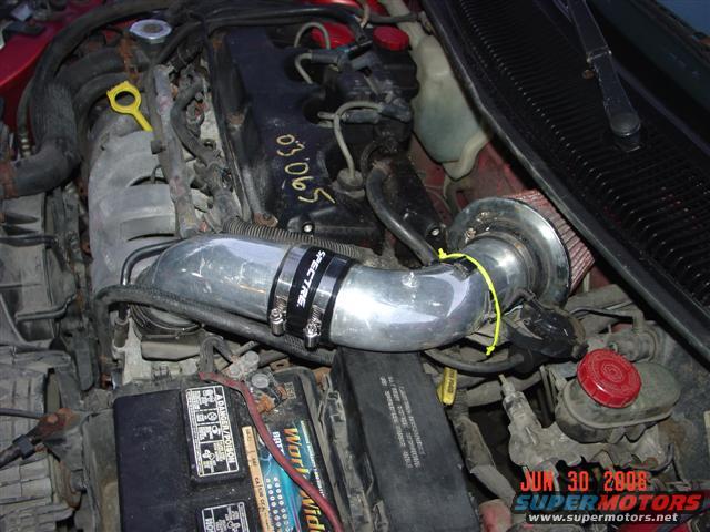 Engine bay with a red car, showing a Spectre air intake system, battery, and brake fluid reservoir