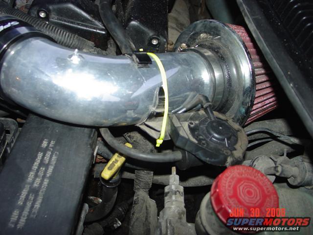 Close-up of an aftermarket air intake with a red filter, connected to engine components. A yellow zip tie secures the intake tube