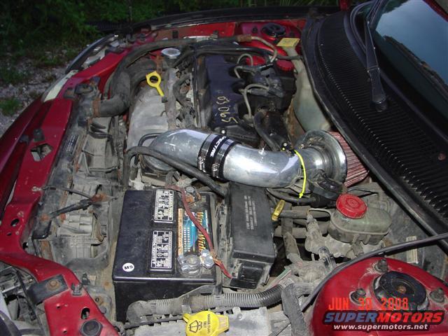 Red engine bay with aftermarket intake and visible battery
