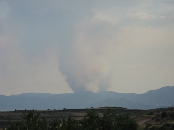 Smoke plumes rise from behind mountains under a hazy sky
