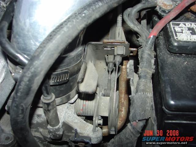 Close-up of engine components including throttle body, cables, and battery