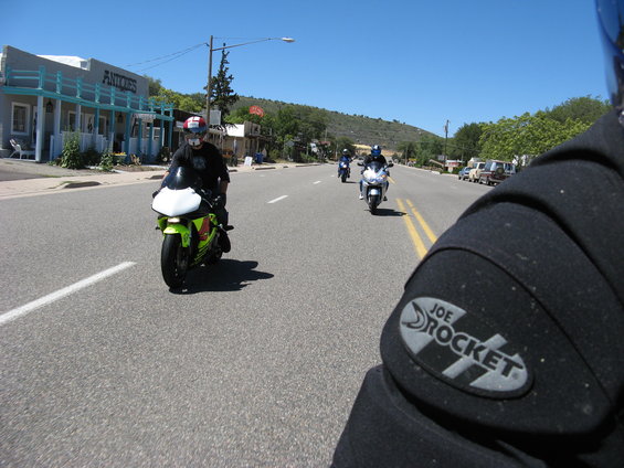 motorcycle rider's perspective looking at a group of bikes on a road with buildings on the side