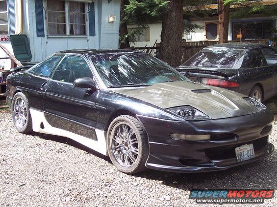 Black Ford Probe with a grey hood and custom body kit, parked on gravel
