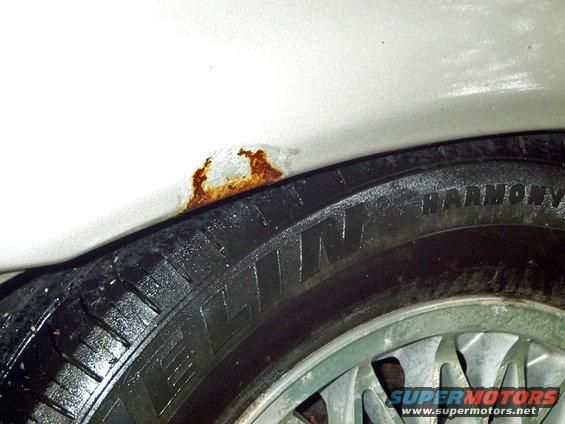 Close-up of rust in wheel well over a tire with 'HARMONY' visible