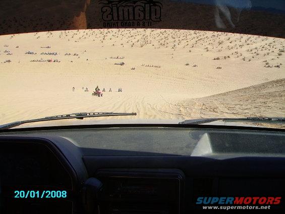 Interior view of a vehicle in sand dunes with ATVs and other vehicles visible