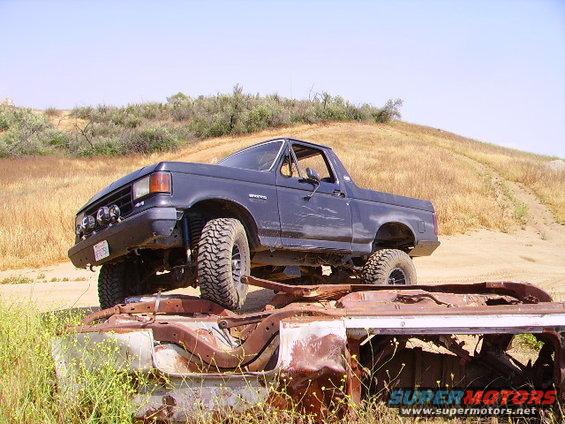 Dark blue Ford Bronco with off-road tires parked on top of a rusted car frame