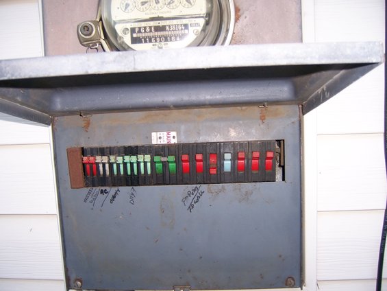 Gray metal electrical panel with circuit breakers and a utility meter above