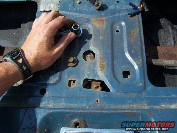 Hand with a socket wrench working on a blue, rusty metal panel with visible bolts and holes