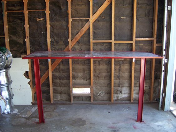 Red metal table with a speckled top, set up in a garage with exposed insulation and wooden studs
