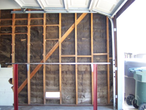 garage interior showing exposed wall insulation and framing, with a metal bar supported by red posts