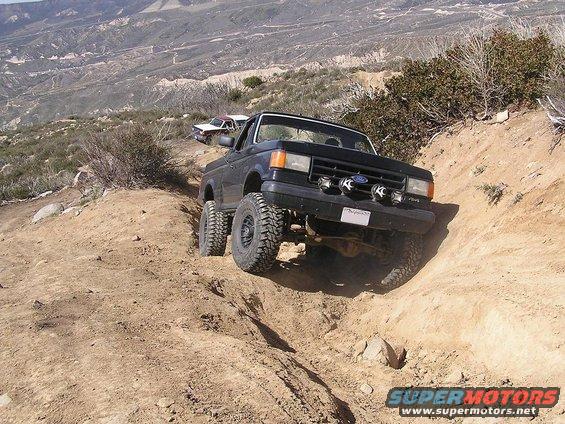 1990 Ford Bronco climbing a steep dirt trail with another vehicle behind it