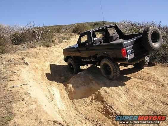 Black Ford Bronco climbing a dirt hill off-road. Spare tire mounted on the back