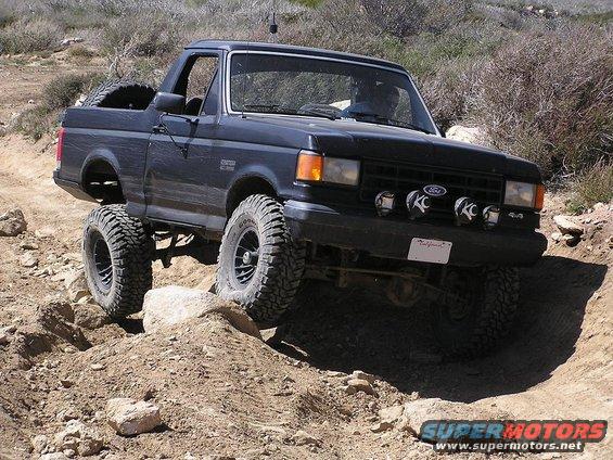 Dark blue Ford Bronco with lifted suspension and off-road tires navigating a rocky trail